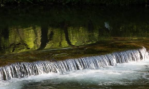 Water flowing over a smooth rock ledge in a green river